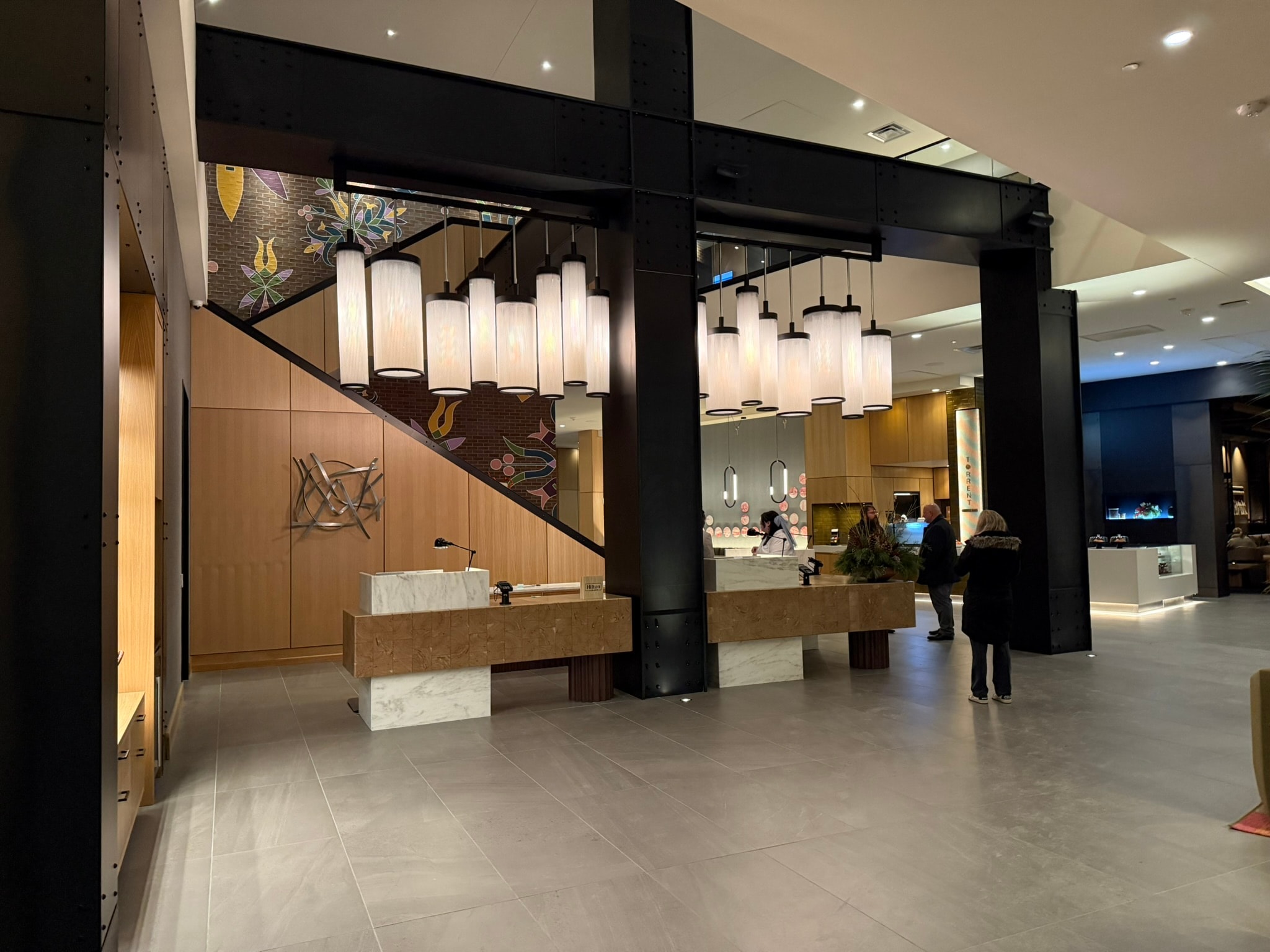 Hotel lobby lounge with communal table, brick fireplace, and coffered wood ceiling