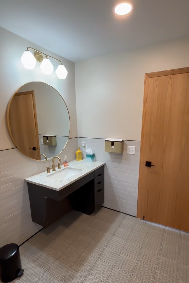Covington restroom with floating vanity, round mirror, and brass fixtures
