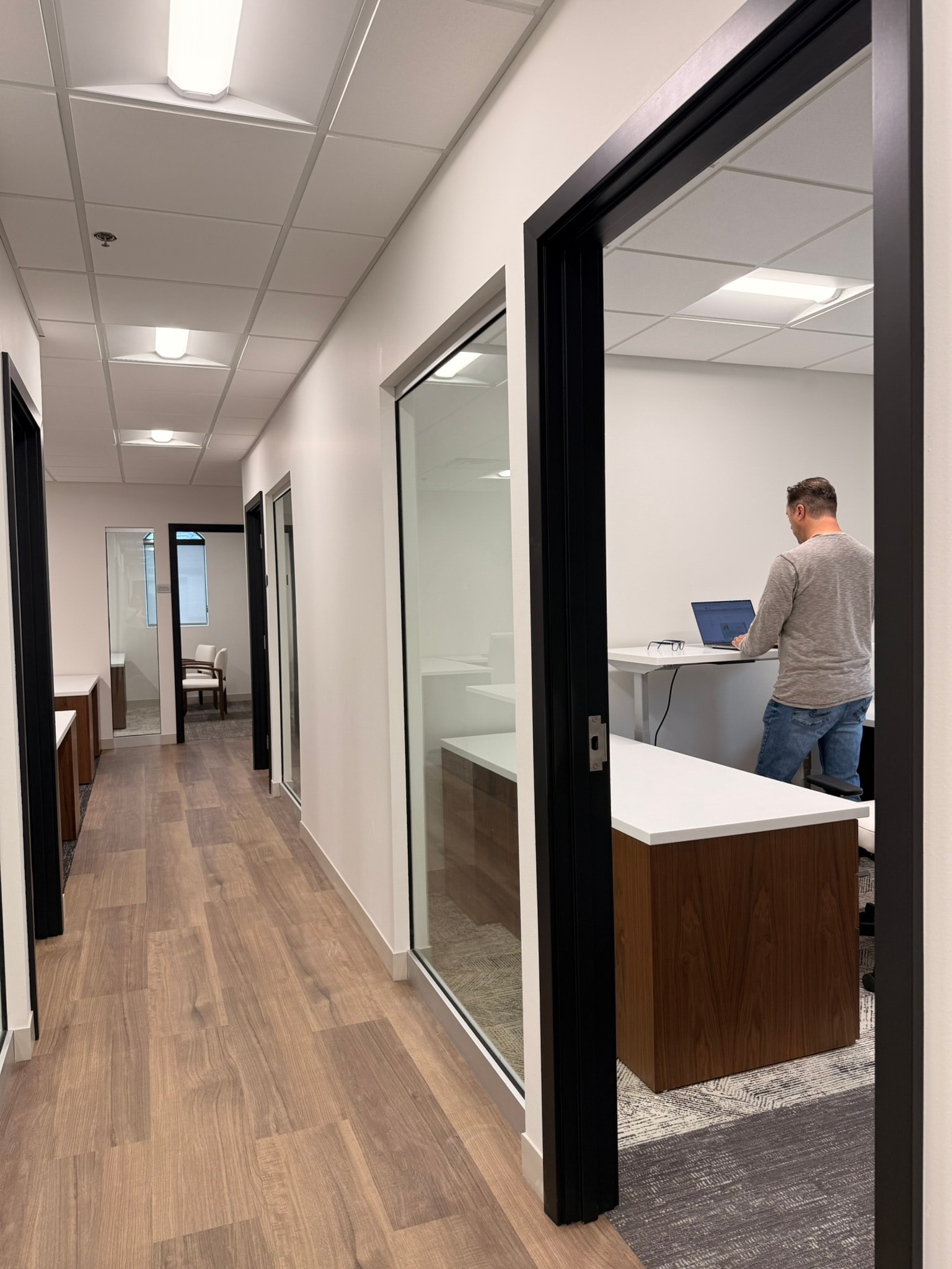 Green Wealth hallway with glass office partitions and standing-desk workspace