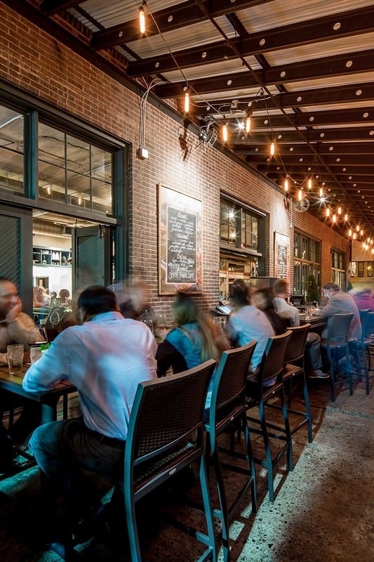 Borough - covered outdoor patio with string lights and brick wall at dusk