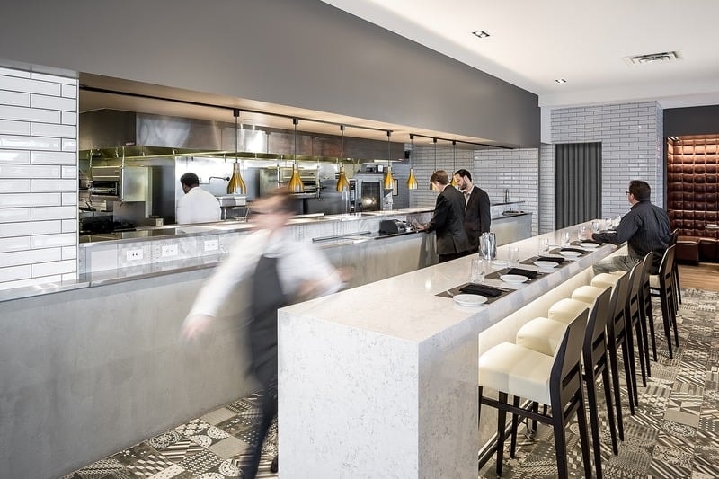 Lela Restaurant - kitchen counter with gold pendants, white tile, and patterned floor
