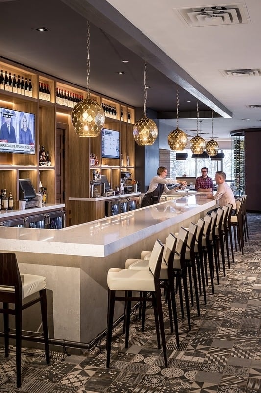 Lela Restaurant - bar with warm wood cabinetry, gold pendant lights, and patterned carpet