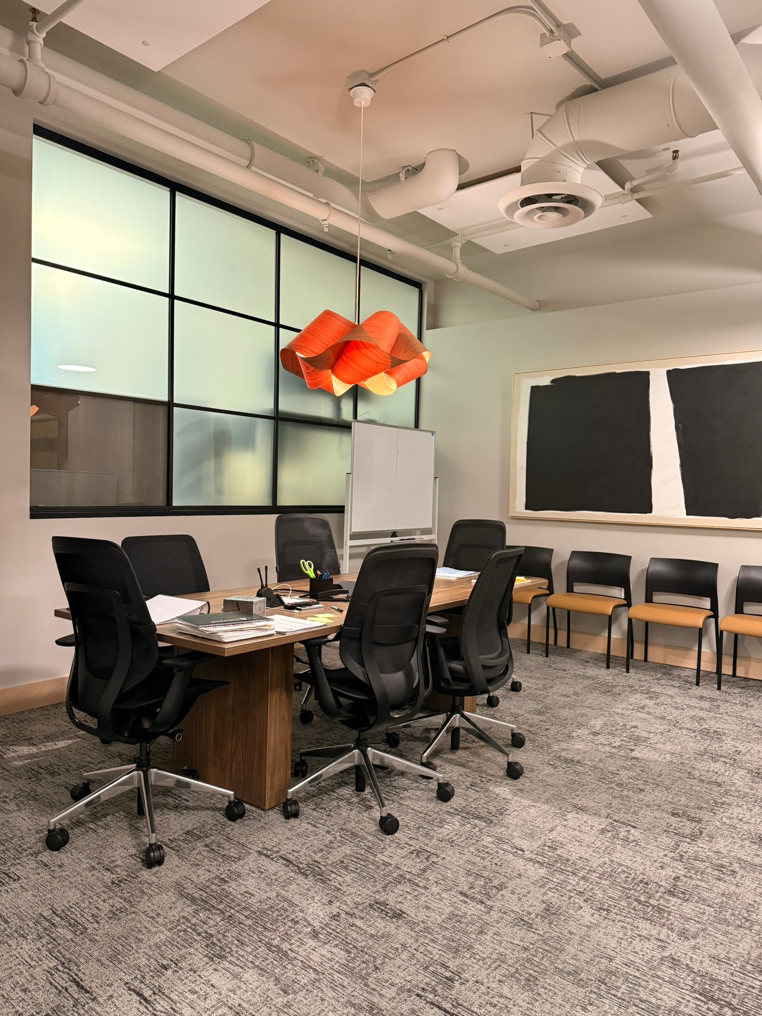 SnowPine Private Wealth conference room with walnut table, black task chairs, orange sculptural pendant, and frosted glass wall