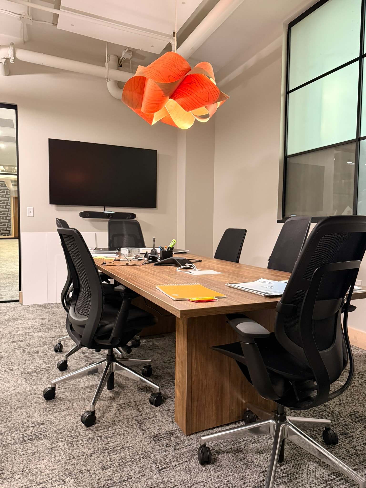 SnowPine Private Wealth conference room with walnut table, black task chairs, and orange sculptural pendant light