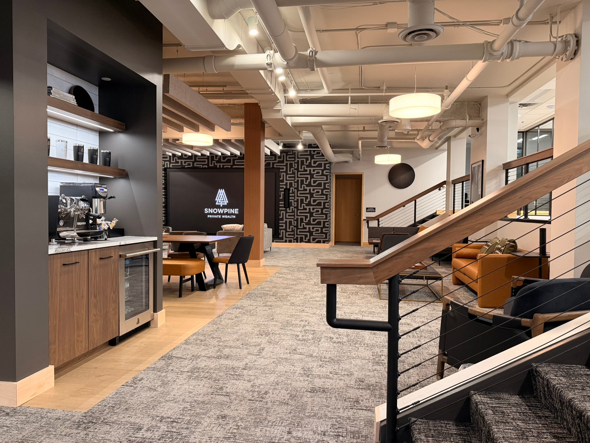 SnowPine Private Wealth main floor with coffee bar, communal dining table, cable-rail staircase, and lounge seating