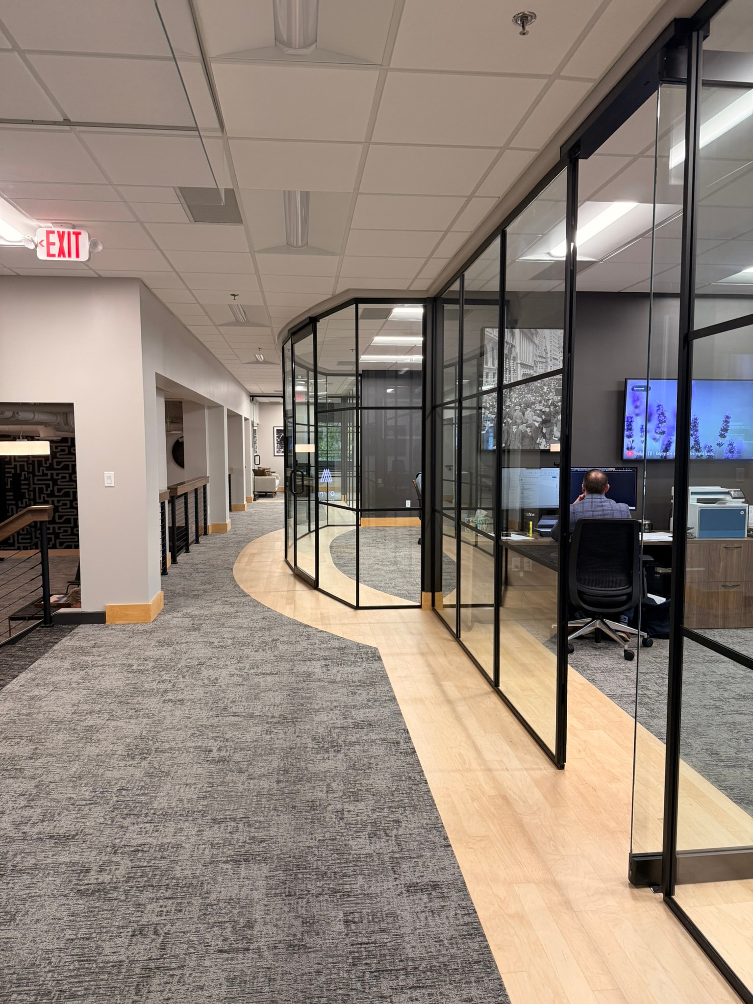 SnowPine Private Wealth upper floor corridor with curved black-framed glass office partitions and wood LVP transition