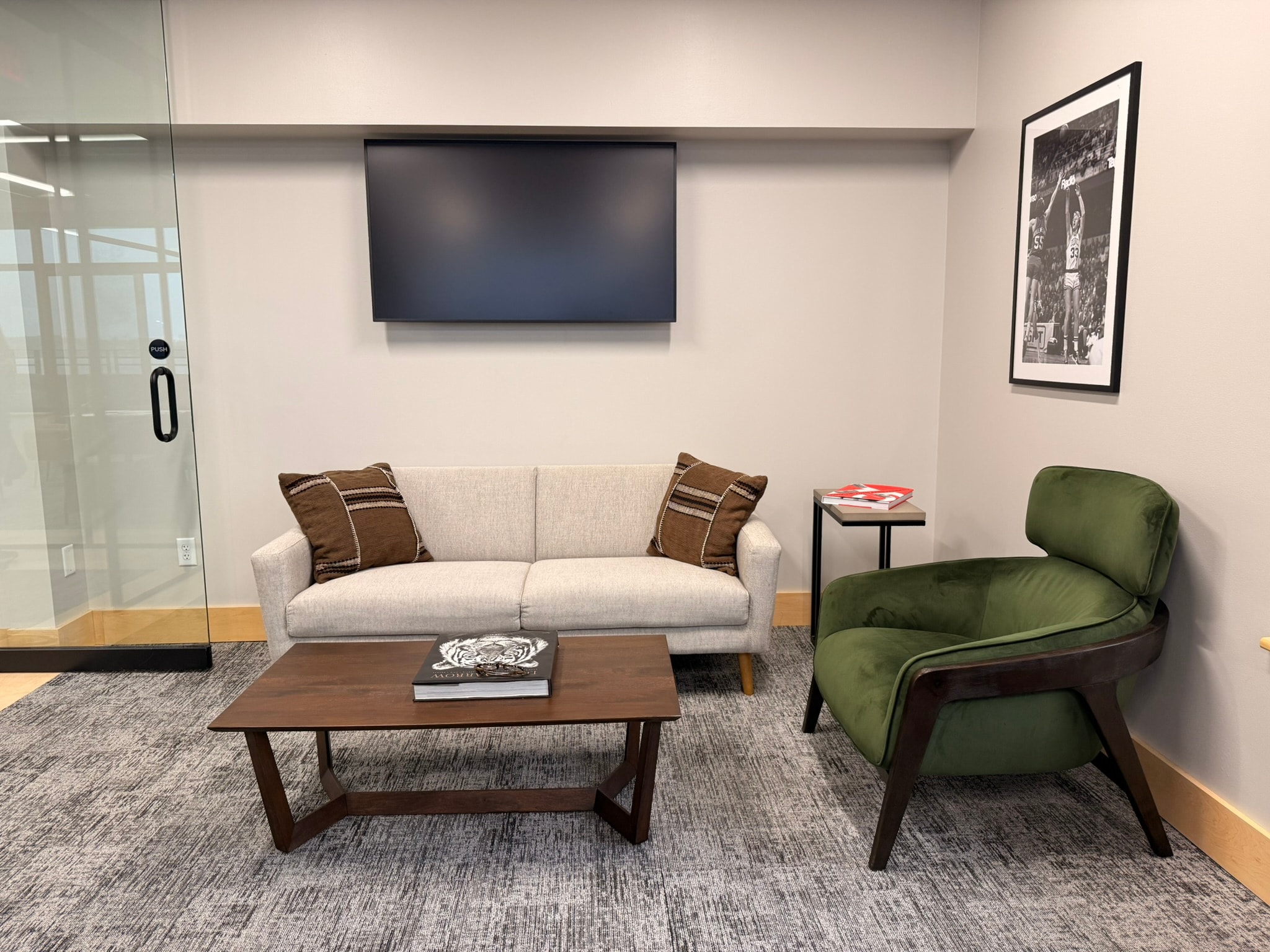 SnowPine Private Wealth client meeting room with linen sofa, green velvet chair, walnut coffee table, and sports photography
