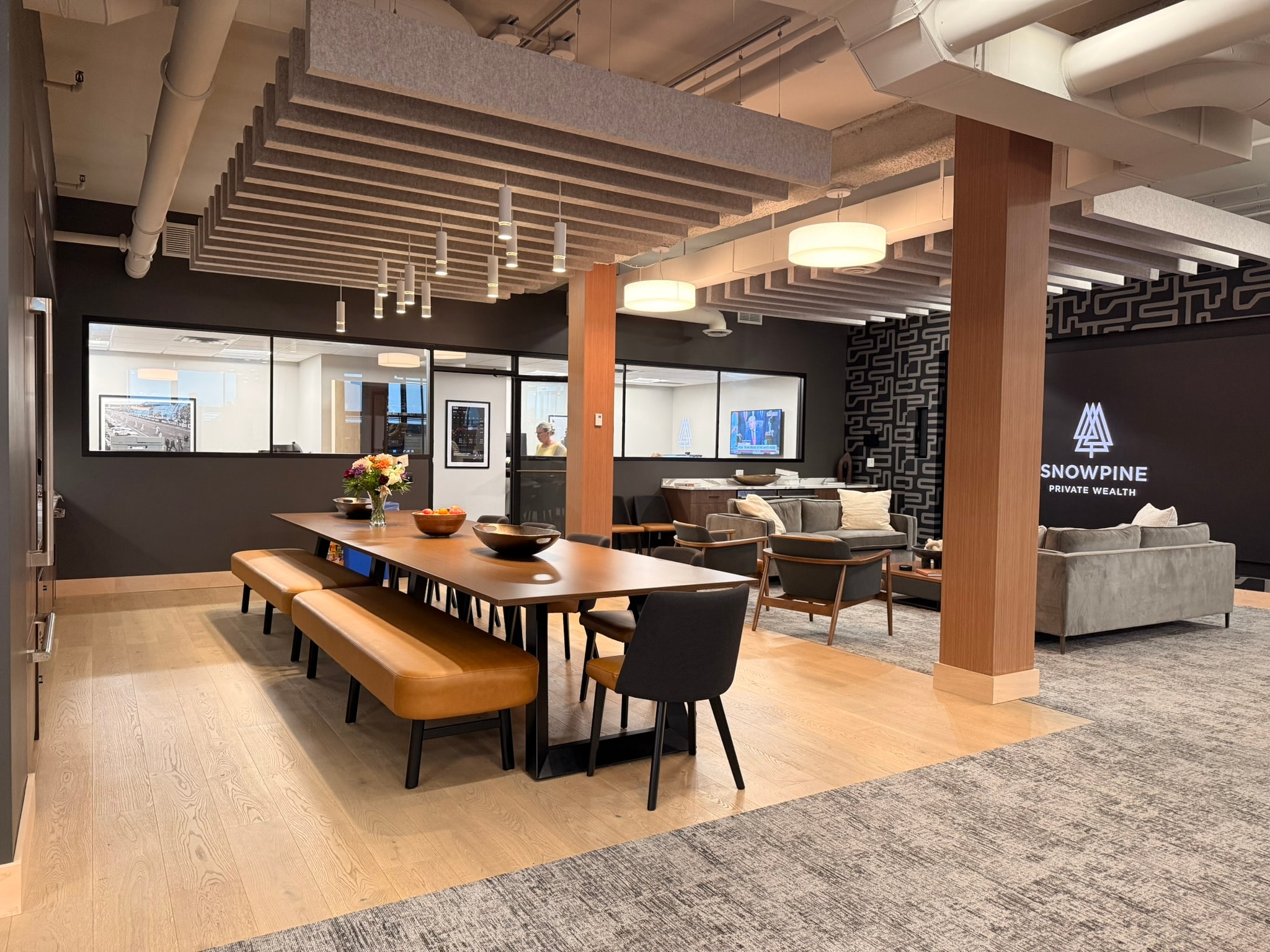 SnowPine Private Wealth main floor communal table with acoustic ceiling baffles, pendant lights, and lounge seating beyond