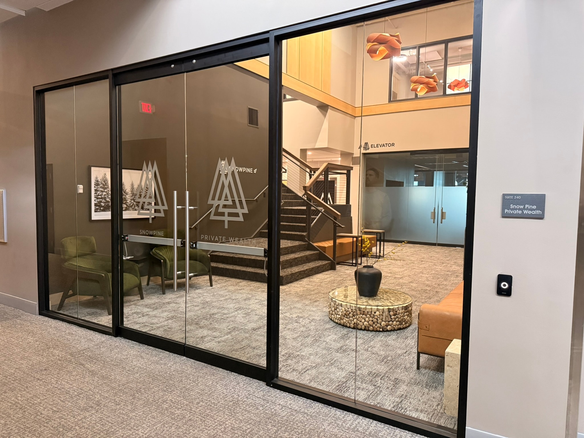 SnowPine Private Wealth glass storefront with etched logo, leather lounge seating, and stairwell beyond