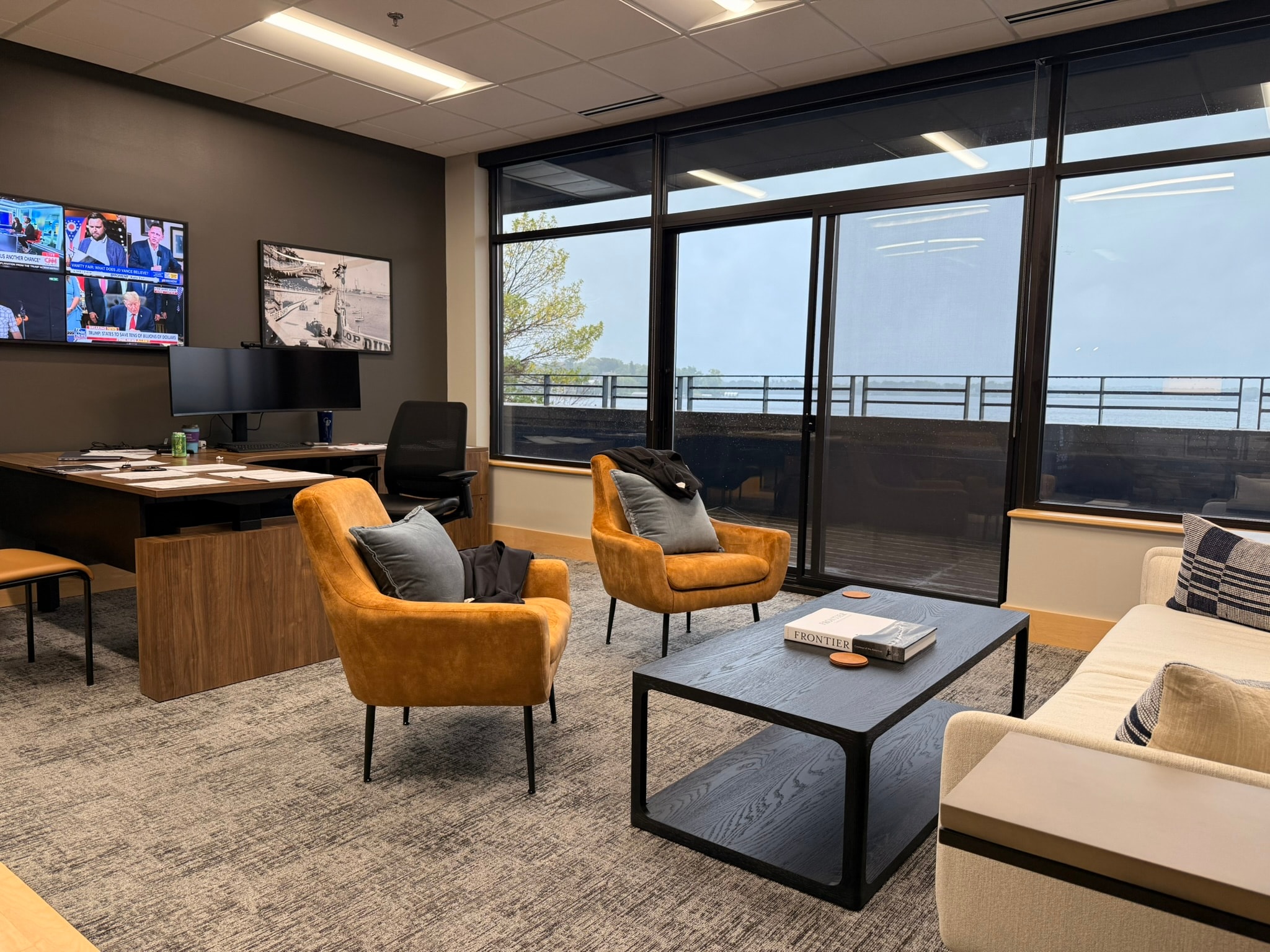SnowPine Private Wealth executive office with amber lounge chairs, dark coffee table, walnut desk, and panoramic lake view