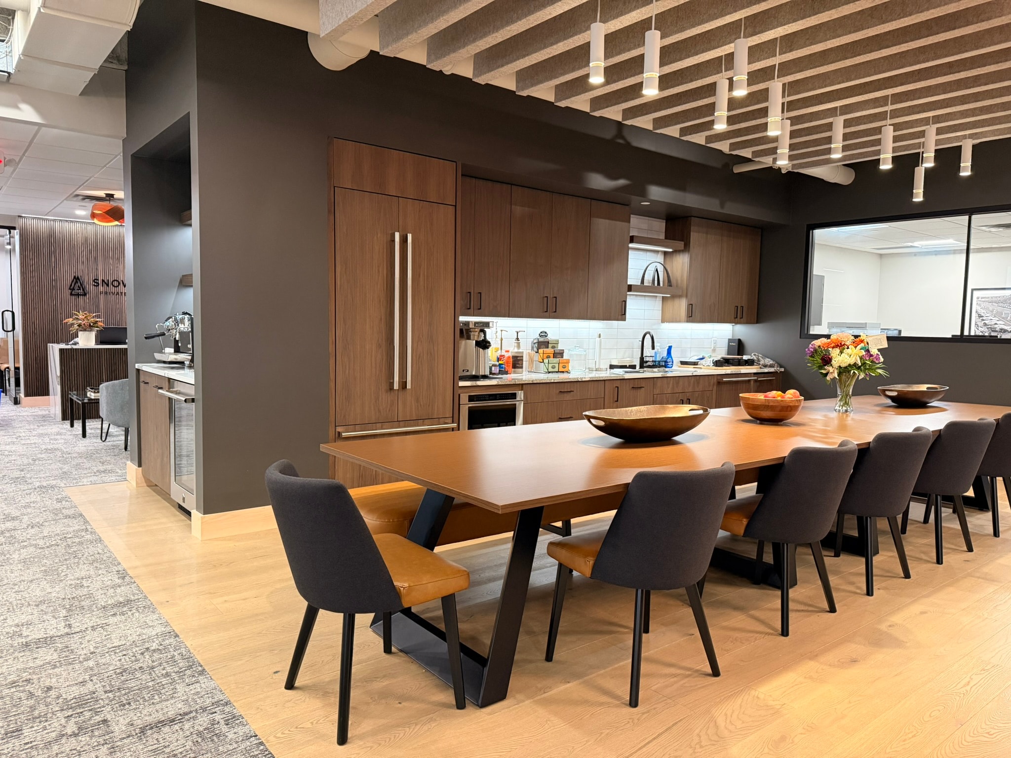 SnowPine Private Wealth kitchen and communal dining area with walnut cabinetry, stainless appliances, and long dining table