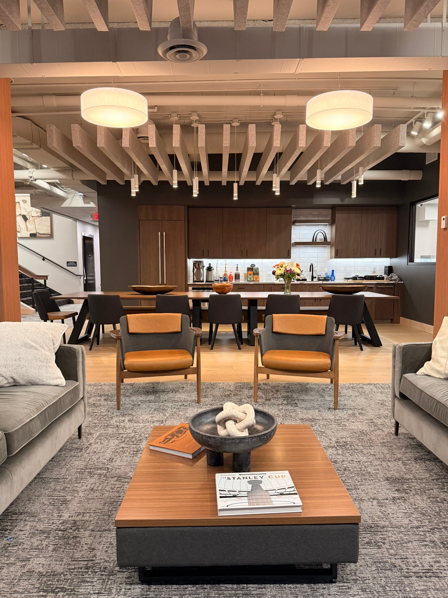 SnowPine Private Wealth main floor lounge with amber leather chairs, communal dining table, kitchen beyond, and cable-rail staircase