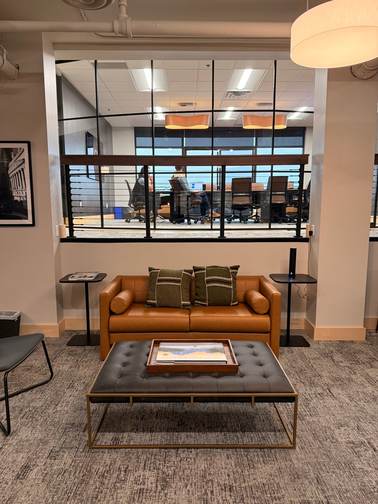 SnowPine Private Wealth lower lounge with cognac leather sofa, tufted ottoman, and glass view into upper conference room