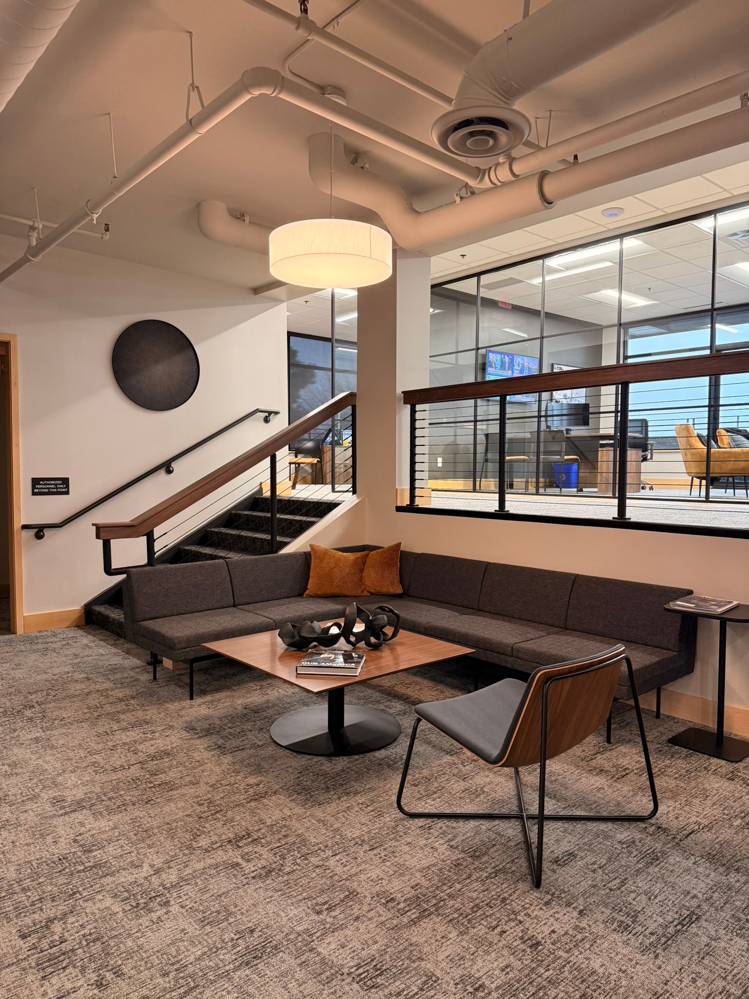 SnowPine Private Wealth lower lounge with L-shaped sectional, cable-rail staircase, and upper floor glass rail beyond