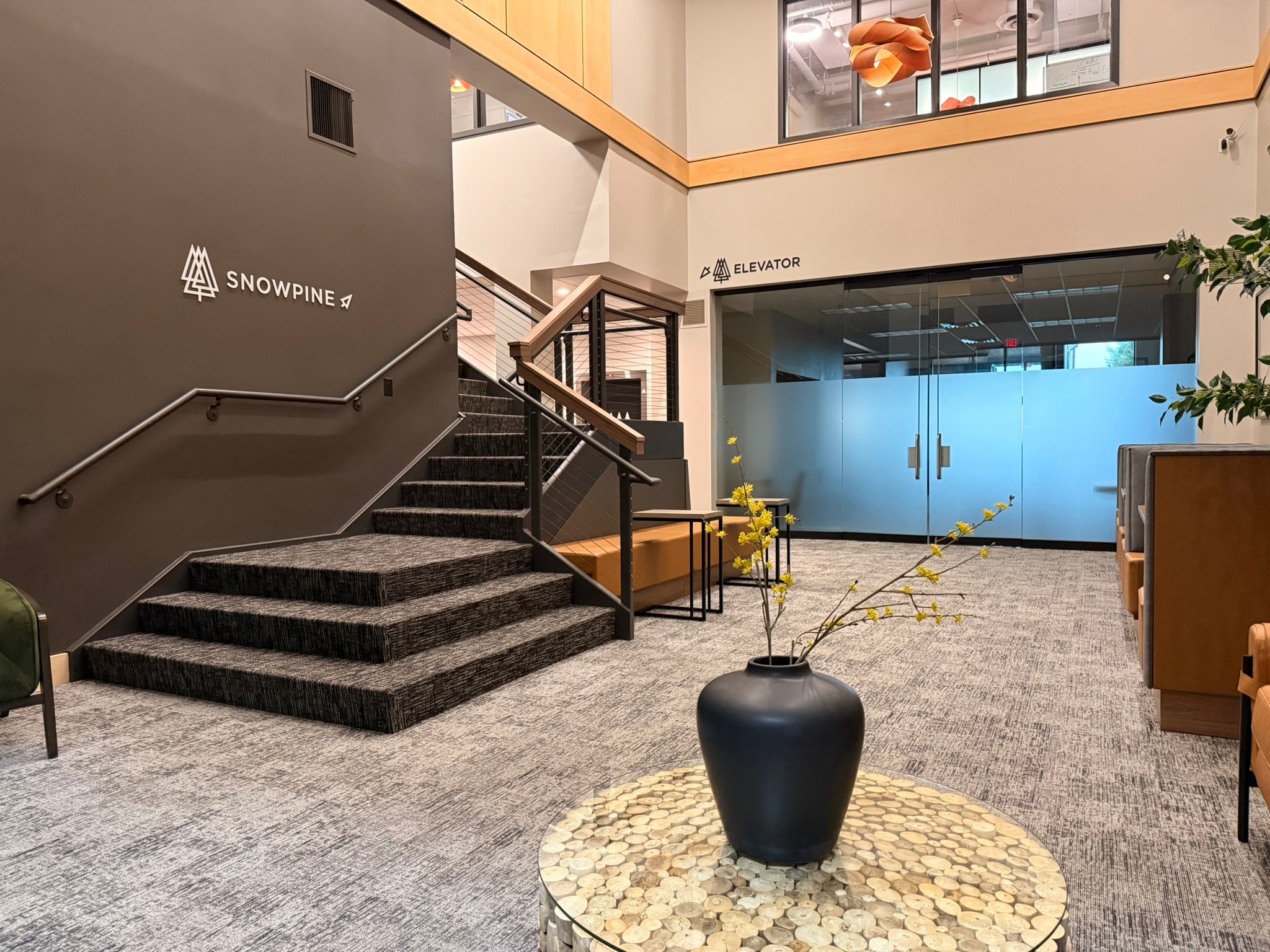 SnowPine Private Wealth atrium stairwell with charcoal accent wall, logo signage, and cable-rail balustrade