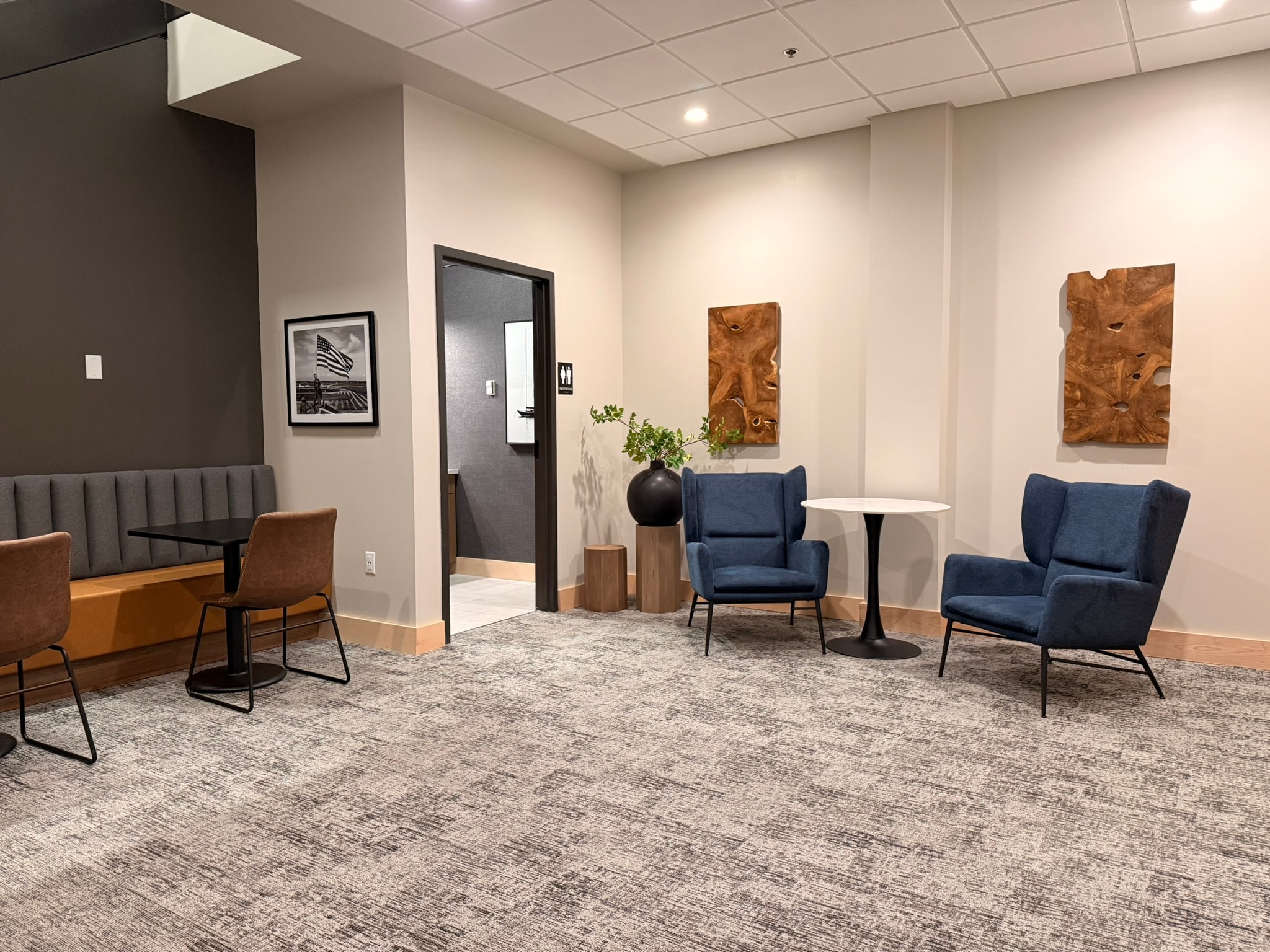 SnowPine Private Wealth lounge alcove with blue wing chairs, teak wall panels, and black vase with greenery