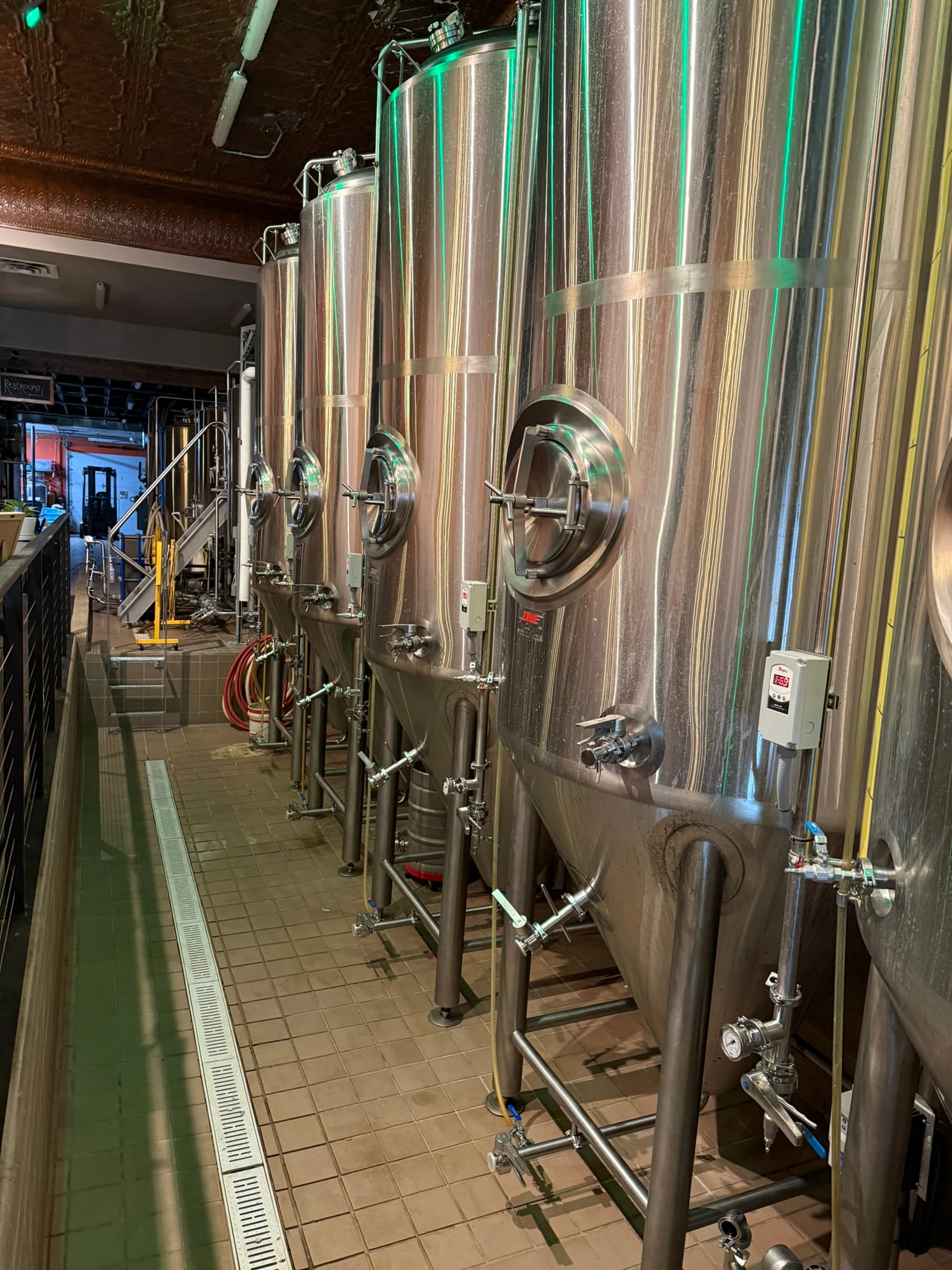 Spiral Brewery production floor with row of stainless fermentation tanks and green accent lighting